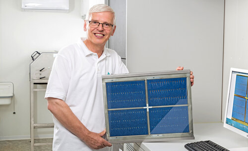 A person holds a frame containing rows of seed samples in front of a camera.